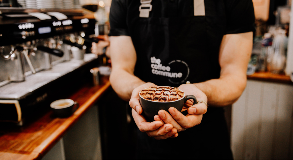 close up of coffee held by a barista wearing the coffee commune apron