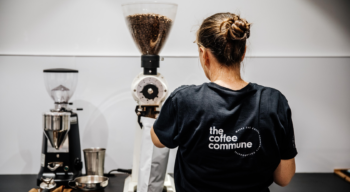 woman in coffee commune tshirt her back facing camera putting roasted coffee in a bag